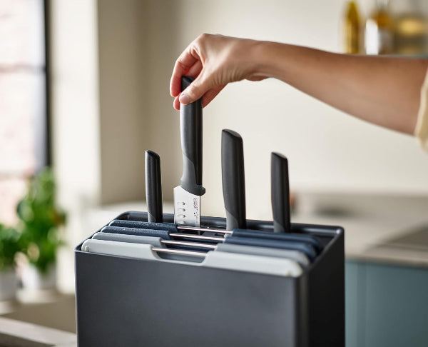 Person inserting a knife into a black knife block on a kitchen counter.