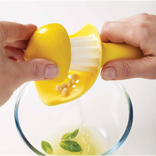 Person using a yellow lemon squeezer over a glass bowl with lemon juice and mint leaves.