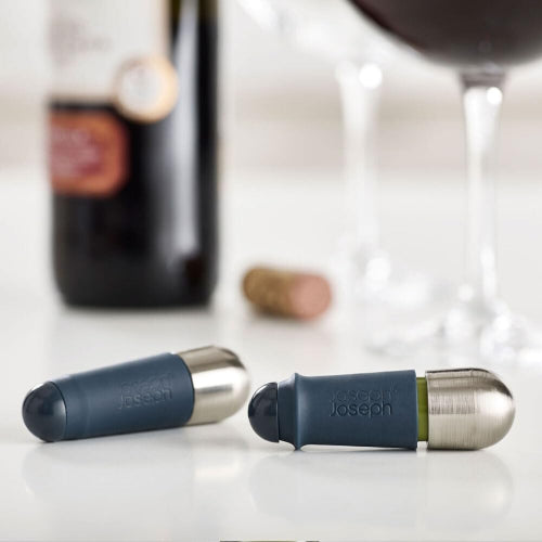 Two Joseph Joseph bottle seals on a surface with a blurred background of a bottle and cork.