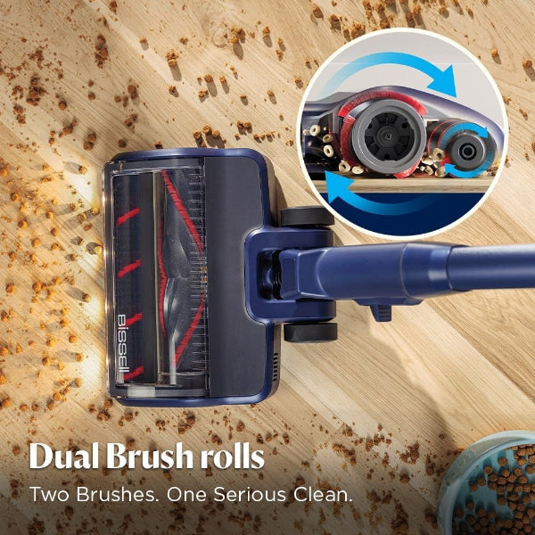 A blue and black Bissell PS318 stick vacuum cleaner shown on a light wood floor with scattered pet food, plus a circular inset showing the dual brush roll mechanism in detail.