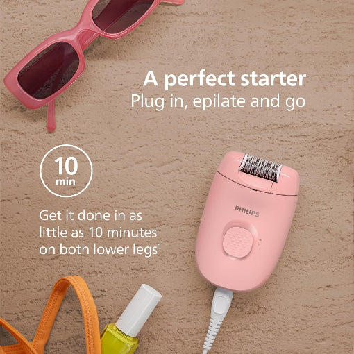 Pink Philips epilator with sunglasses, bottle, and bag on a wooden surface